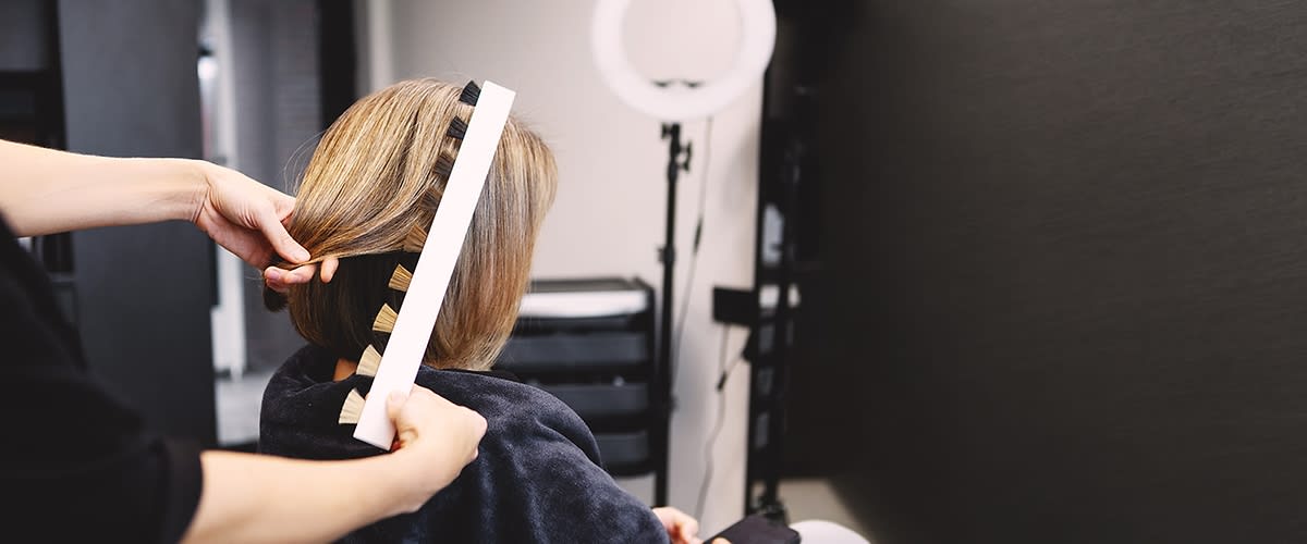 Friseurin misst mit Streifenlineal die Länge eines kinnlangen blonden Haarschnitts bei Kundin im Salon