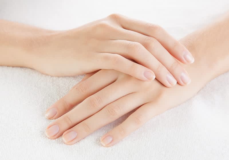 Zwei gepflegte Hände liegen flach übereinander auf einem weißen Handtuch, Fingernägel kurz und naturbelassen, glatte Haut