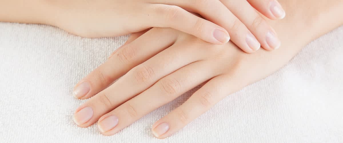 Zwei gepflegte Hände liegen flach übereinander auf einem weißen Handtuch, Fingernägel kurz und naturbelassen, glatte Haut