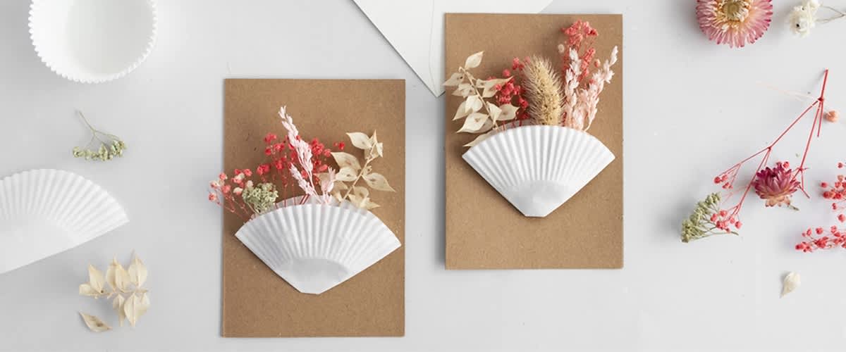 Zwei braune Karten mit weißen Papierfächern, gefüllt mit getrockneten Blumen in Rot, Weiß und Beige.