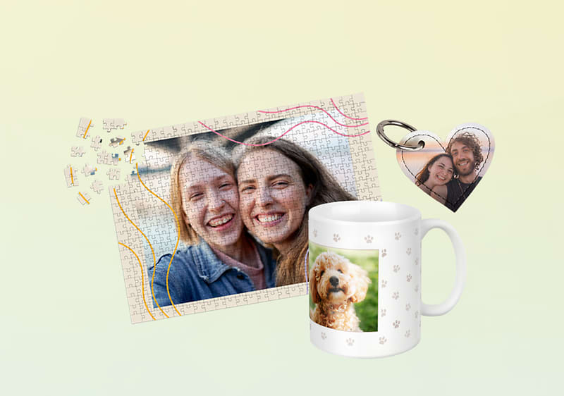 Fotopuzzle mit zwei Personen, daneben ein weißer Fotobecher mit einem Bild eines kleinen, lockigen Hundes und Pfotenmuster sowie ein herzförmiger Schlüsselanhänger mit Foto neben dem Puzzle