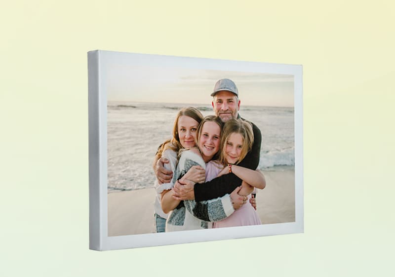 Leinwandfoto mit einer umarmenden Familie aus zwei Erwachsenen und zwei Kindern am Strand bei Sonnenuntergang, gedämpfte Farben, weiße Rahmenkante