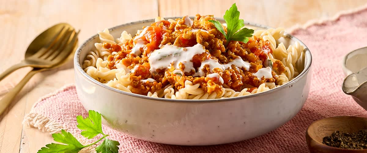 Schale mit Spiralnudeln, darüber Sauce mit Hackfleisch, etwas weißer Crème und ein Petersilienzweig