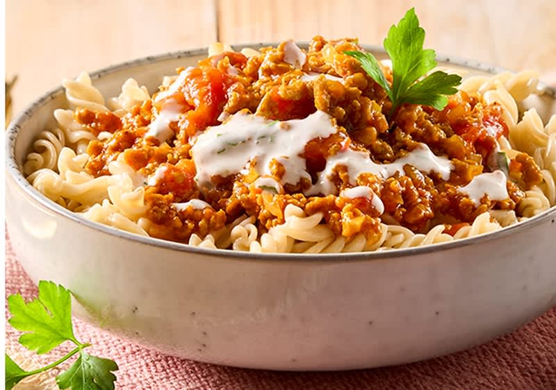 Schale mit Spiralnudeln, darüber Sauce mit Hackfleisch, etwas weißer Crème und ein Petersilienzweig