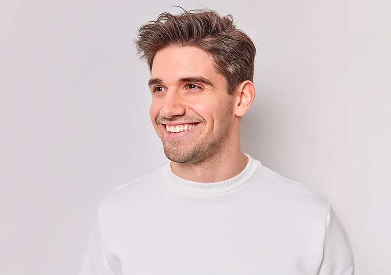 Mann mit kurz gestyltem Haar trägt ein weißes Sweatshirt vor hellem Hintergrund