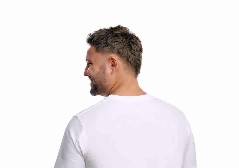Mann von hinten und leicht seitlich, trägt ein weißes T‑Shirt und blickt über die rechte Schulter hinweg
