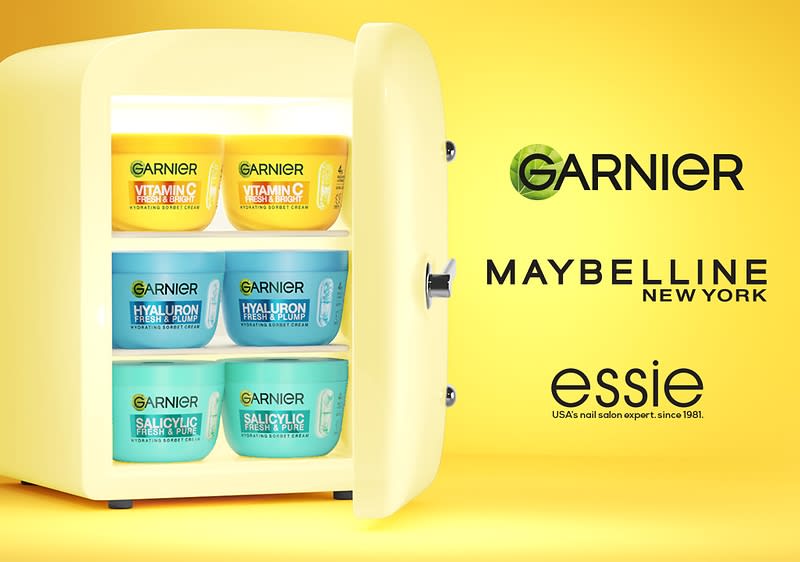 Kleiner gelber Kühlschrank geöffnet mit sechs Garnier-Gesichtsmasken in drei Varianten auf drei Regalen und rechts Logos von Garnier, Maybelline, essie