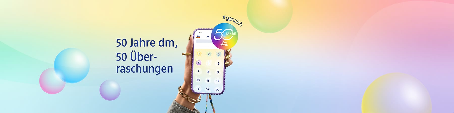 Bunte Werbegrafik zum Jubiläum: Links der Text „50 Jahre dm, 50 Überraschungen“, rechts eine Hand mit Schmuck hält ein Smartphone mit Zahlenfeld 1–15, oben rechts rundes Logo „50 Jahre dm“ mit dem Hashtag „#ganzich“