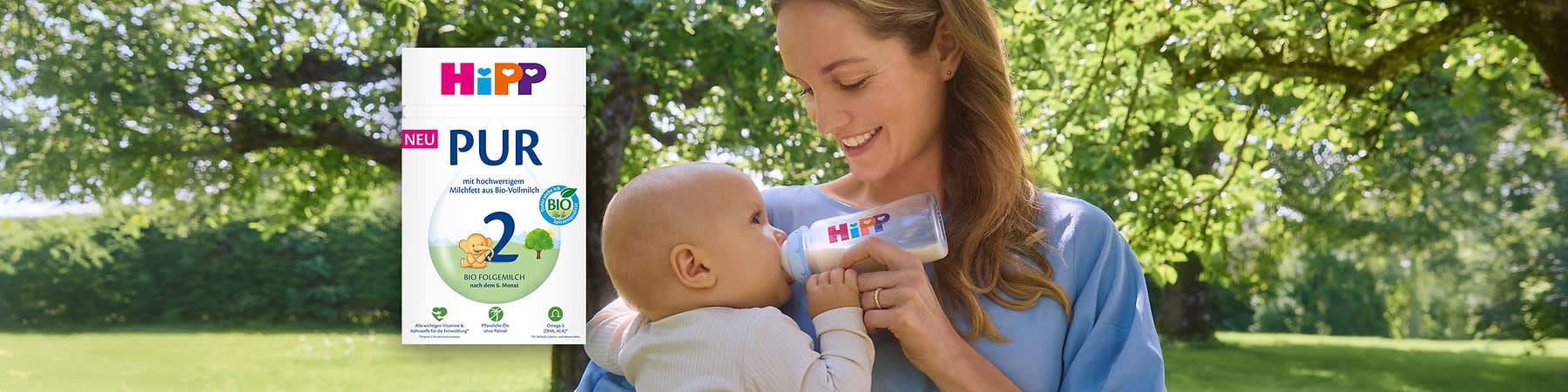 HiPP PUR Folge 2 Bio-Milchpulver-Packung in Weiß mit buntem HiPP-Logo, großer blauer Zahl 2, Aufschrift „PUR“ und „NEU“ sowie Bio-Siegel auf grünem Gartentisch ohne Punkt