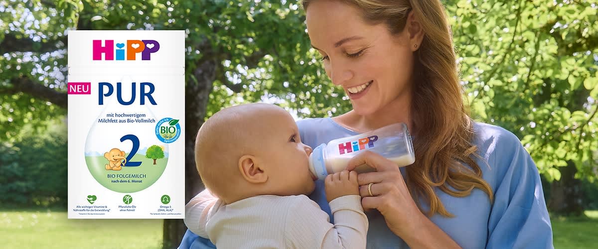 HiPP PUR Folge 2 Bio-Milchpulver-Packung in Weiß mit buntem HiPP-Logo, großer blauer Zahl 2, Aufschrift „PUR“ und „NEU“ sowie Bio-Siegel auf grünem Gartentisch ohne Punkt