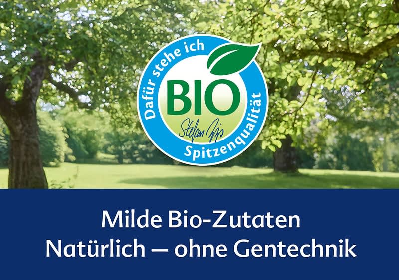 Grünes Parkgelände mit Bäumen oben, mittig rundes grünes-blaues Bio-Siegel mit Blatt und Schrift „BIO Spitzenqualität“, unten blauer Balken mit weißer Aufschrift „Milde Bio-Zutaten Natürlich – ohne Gentechnik“