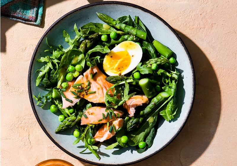 Teller mit grünem Spargel, Erbsen und Rucola, dazu Lachsfiletstücke und ein halbiertes weich gekochtes Ei