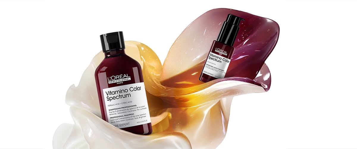 Zwei dunkelrote L'Oréal Professionnel Vitamino Color Spectrum Shampoo- und Serumflaschen auf geschwungenen perlmuttfarbenen und goldenen Blütenblättern