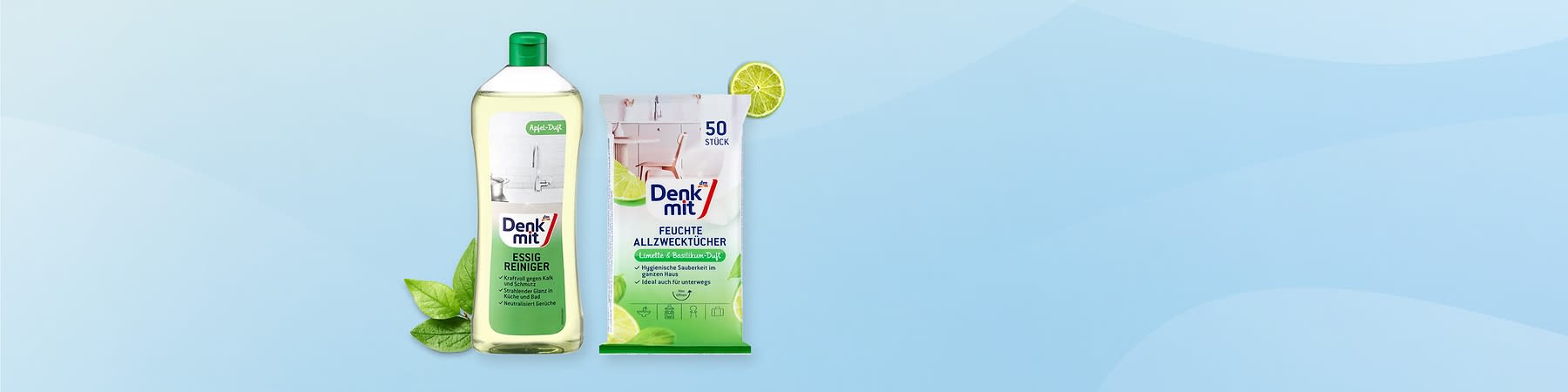 Eine gelbliche Flasche Essigreiniger von Denkmit mit grünem Verschluss neben einer Packung feuchter Allzwecktücher von Denkmit mit der Aufschrift „50 Stück“, Limettenscheiben und grünen Blättern im Hintergrund