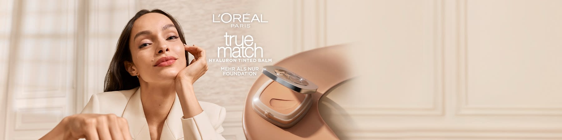 Werbetext für L'Oréal Paris True Match Hyaluron Tinted Balm über einem Foto einer elegant gekleideten Frau im cremefarbenen Blazer, rechts eine offene Puderdose mit beige-farbenem Tinted Balm und dem Schriftzug „L'ORÉAL PARIS true match HYALURON TINTED BALM MEHR ALS NUR FOUNDATION“