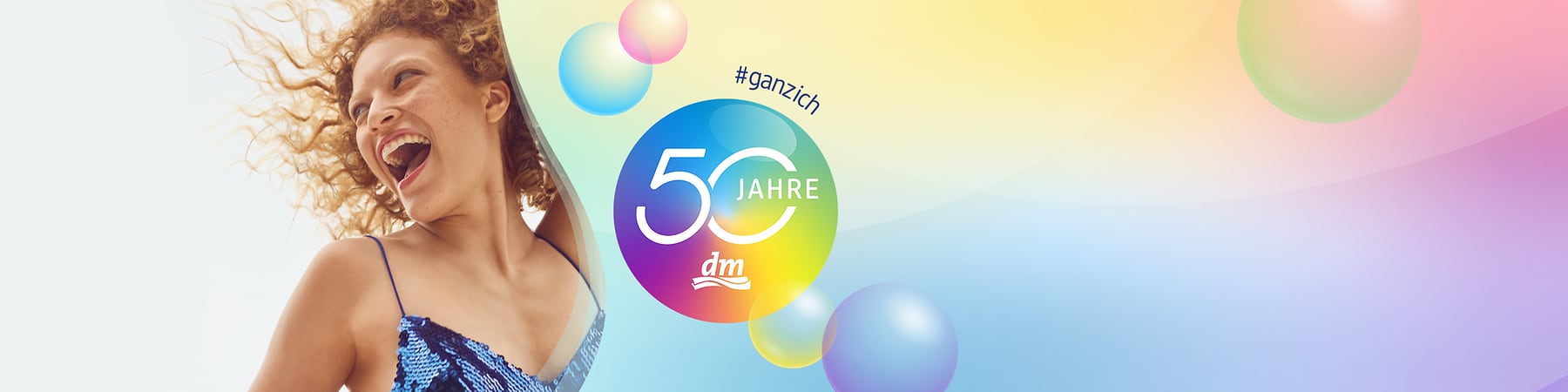 Frau in blau schimmerndem Paillettenkleid mit lockigem Haar, daneben bunter Kreis mit Text „50 Jahre“ und dm-Logo, Hashtag „#ganzich“