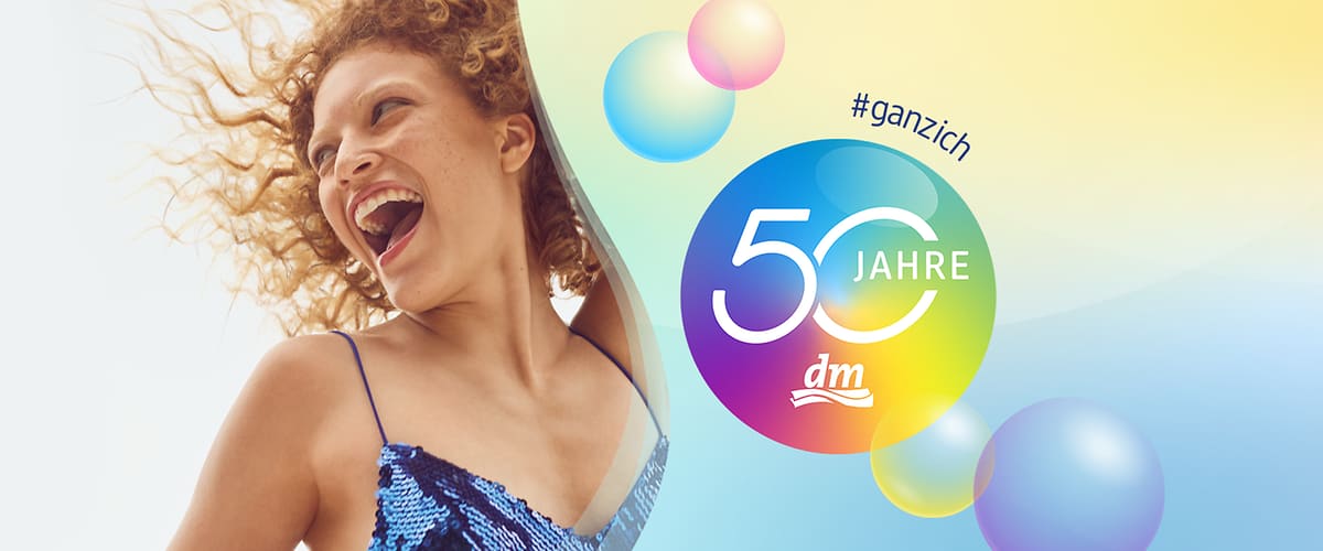Frau in blau schimmerndem Pailletten-Top, lockiges Haar, daneben bunter Kreis mit Schrift „50 Jahre“ und dm-Logo sowie Hashtag „#ganzich“