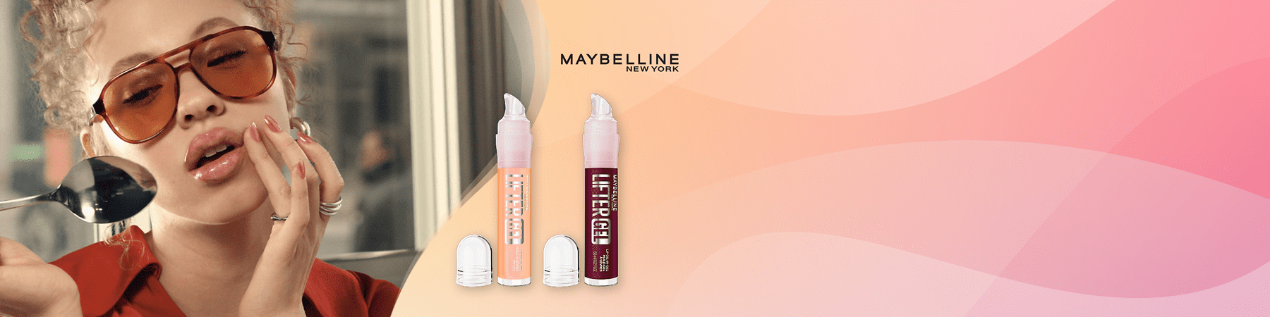 Zwei Maybelline Lift Gel Lippenpflege-Flakons in hellrosa und dunkelrot vor einem roséfarbenen Verlauf, rechts oben das Maybelline New York Logo, links ein teilweise sichtbarer Oberkörper einer Person mit rotem Hemd und abgeblendeter Gesichtspartie