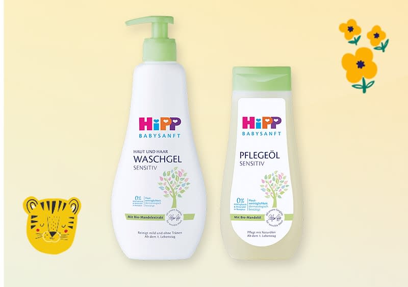 Zwei HiPP Babysanft-Produkte nebeneinander: links weiße Pumpflasche „Haut und Haar Waschgel Sensitiv“, rechts hellgrüne Flasche „Pflegeöl Sensitiv“, jeweils mit Pflanzenmotiv und HiPP-Logo, gelber Hintergrund, rechts oben Blumen und links unten Tiger-Icon