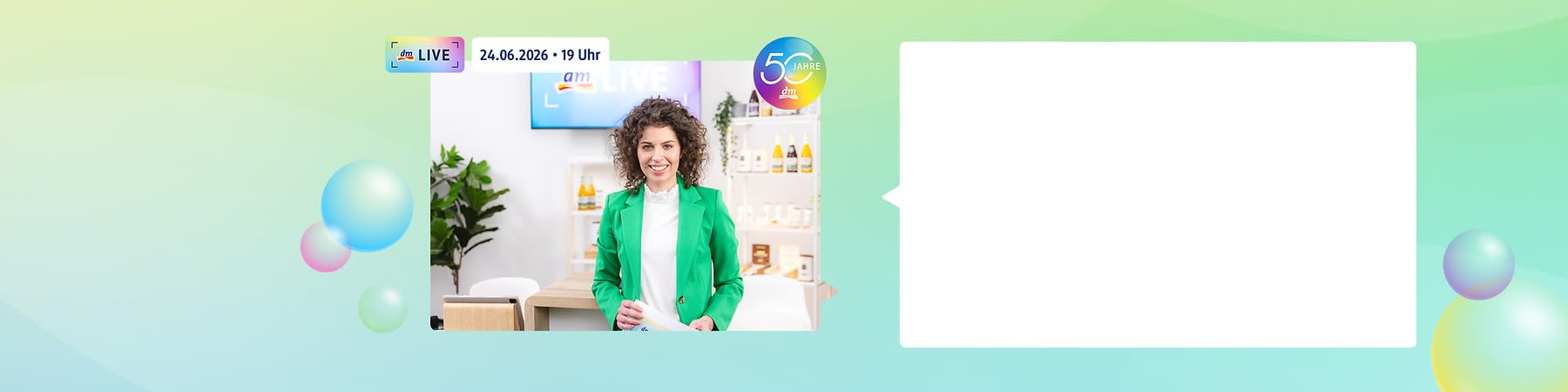 Frau in grünem Blazer steht in einem hellen Studio vor einem Holztisch und hält Papiere, im Hintergrund Regale mit Produkten und ein Bildschirm mit Datum „24.06.2026 • 19 Uhr“ sowie ein runder Schriftzug „50 Jahre dm“
