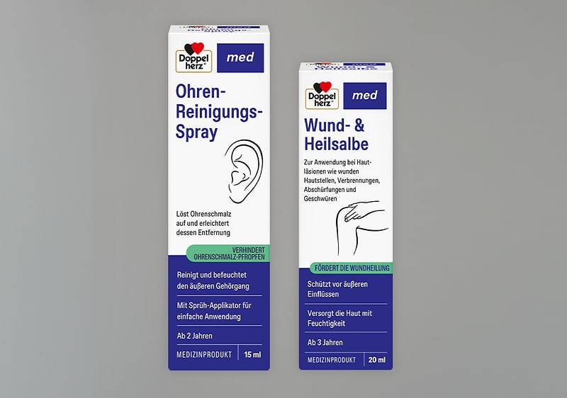 Zwei weiße Produktkartons der Marke Doppelherz nebeneinander; links Ohren-Reinigungs-Spray 15 ml mit Ohrillustration und blauer sowie grüner Textleiste, rechts Wund- & Heilsalbe 20 ml mit Hand-Illustration und blauer sowie grüner Textleiste
