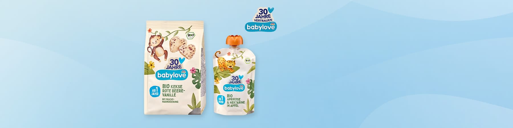 Links eine beige Tüte Babylove Bio-Kekse „Rote Beere-Vanille“ mit Affen-Illustration und Herzkeksen, rechts eine Quetschpackung Babylove Bio „Aprikose & Nektarine in Apfel“ mit Leoparden-Illustration, oben rechts kleines Babylove-Logo mit Schriftzug „30 Jahre Vertrauen“