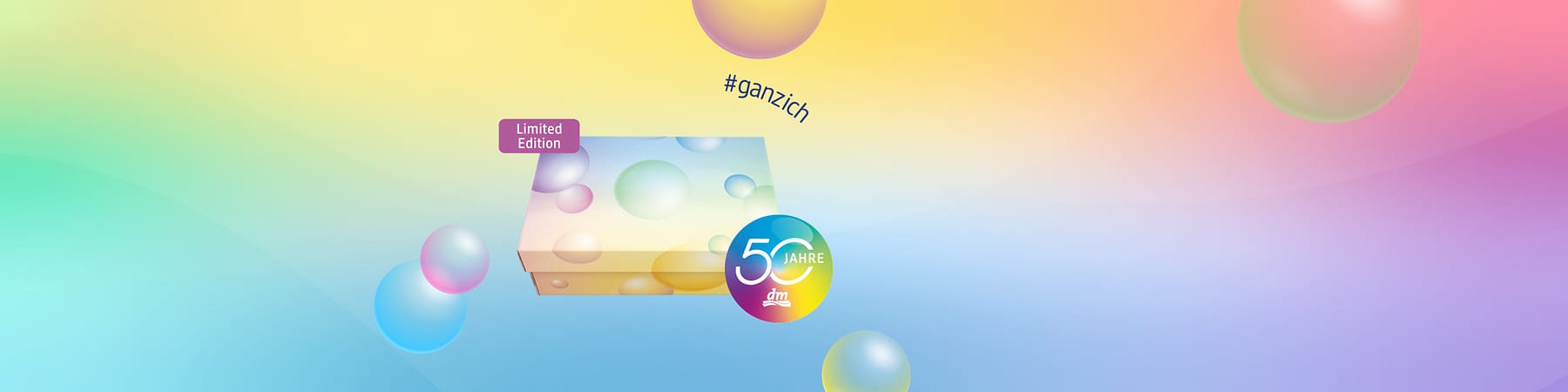 Bunte Geschenkbox mit pastellfarbenen Kugelmotiven, oberes Ecklabel „Limited Edition“ und rundes Emblem „50 Jahre dm“ sowie Hashtag „#ganzich“ im Hintergrund