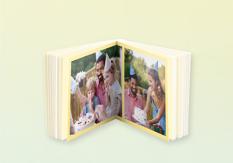 Aufgeschlagenes Fotobuch mit gelben Seitenrändern, links eine Familie mit kleinem Kind und Geburtstagskuchen, rechts ein Mann und eine Frau, die gemeinsam einen Kuchen halten, heller Hintergrund
