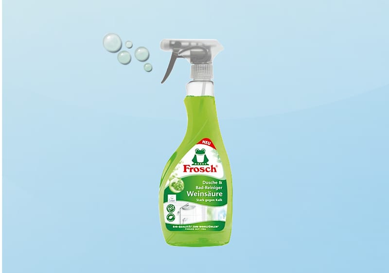 Grüne Sprühflasche des Reinigers „Frosch Dusche & Bad-Reiniger Weisssau­re“ mit Frosch-Logo, Aufschrift „Weiß­säure“ und Piktogramm einer Dusche vor blauem Hintergrund