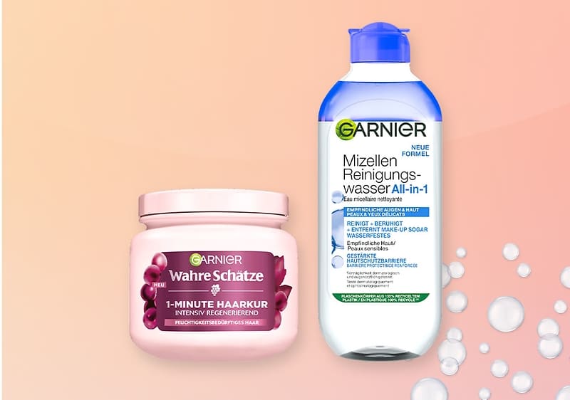Zwei Garnier-Produkte auf pastellrosa Hintergrund: links ein rosa Tiegel „Garnier Wahre Schätze 1-Minute Haarkur intensiv regenerierend“, rechts eine blaue Flasche „Garnier Mizellen Reinigungswasser All-in-1“ mit sichtbaren Blasen neben der Flasche