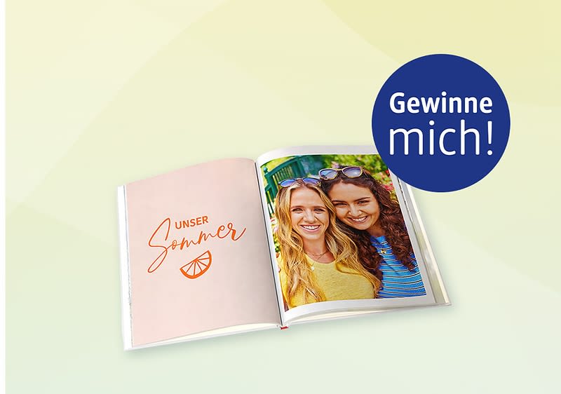 Aufgeschlagendes Fotobuch, linke Seite rosa mit Schrift „UNSER Sommer“ und einer kleinen Orangenscheibe, rechte Seite Foto zweier lächelnder Frauen nebeneinander, oben rechts blauer Kreis mit weißer Aufschrift „Gewinne mich!“