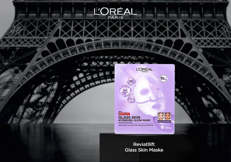 L'Oréal Paris Glass Skin Hydrogel Glow Mask Verpackung in hellem Violett mit Gesichtsmaske-Abbildung und Text „Glass Skin Hydrogel Glow Mask“ vor stilisiertem Eiffelturm im Hintergrund und Produktname „Revitalift Glass Skin Maske“ darunter