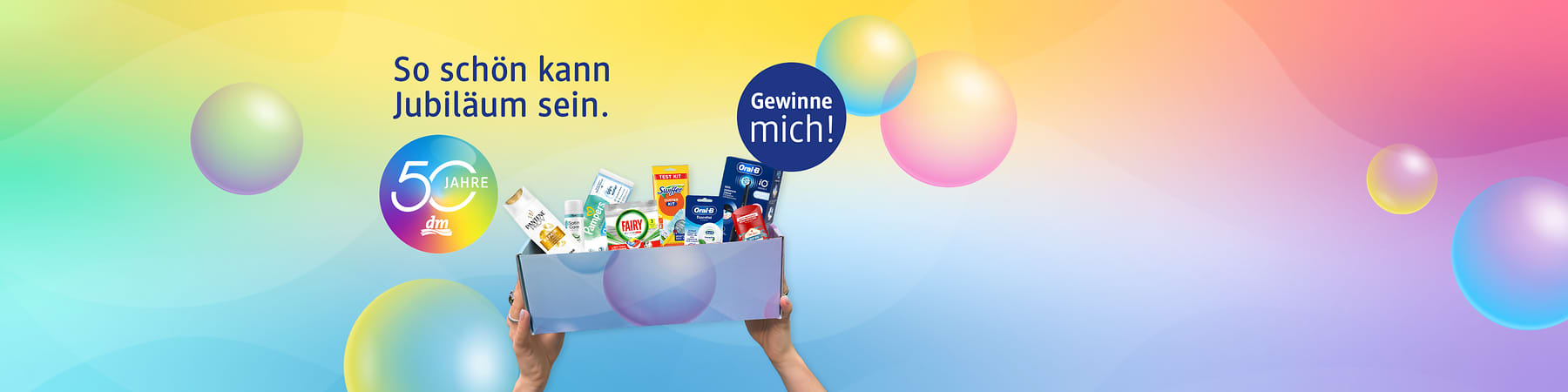 Bunte Jubiläumswerbung mit dem Text „So schön kann Jubiläum sein“, dem runden Logo „50 Jahre dm“ links und einem blauen Kreis rechts mit „Gewinne mich!“, in dessen Mitte Hände eine Geschenkbox mit verschiedenen Drogerieprodukten wie Zahnpasta, Shampoo, Waschmittel und Putzmittel halten