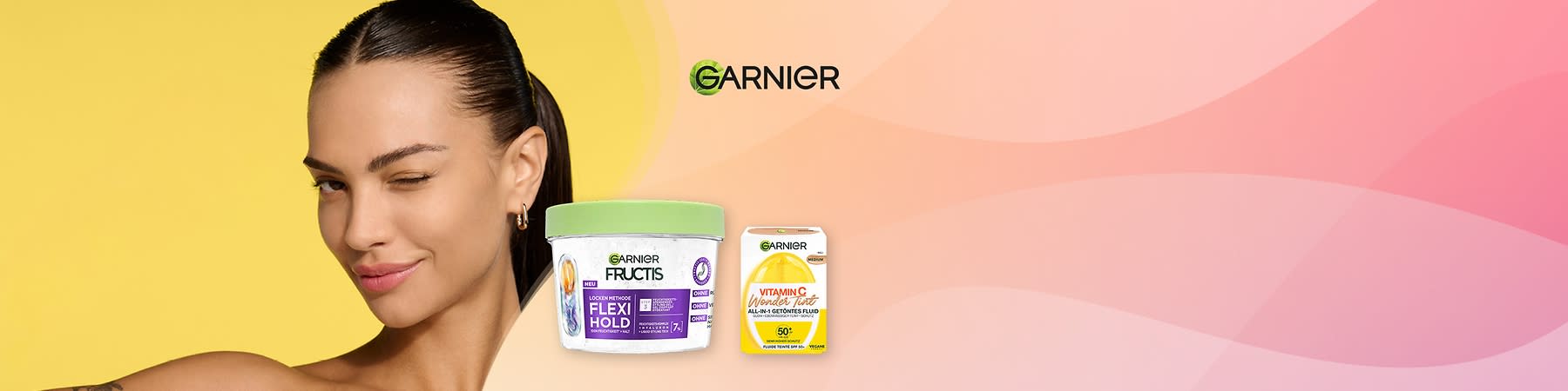 Porträt einer lächelnden Frau mit zurückgebundenem Haar, daneben ein Garnier Fructis Flexi Hold Haarstyling-Topf mit grünem Deckel und lila Etikett sowie eine Garnier Vitamin C Wonder Tint Box mit gelb-weißer Verpackung und Garnier-Logo oben rechts