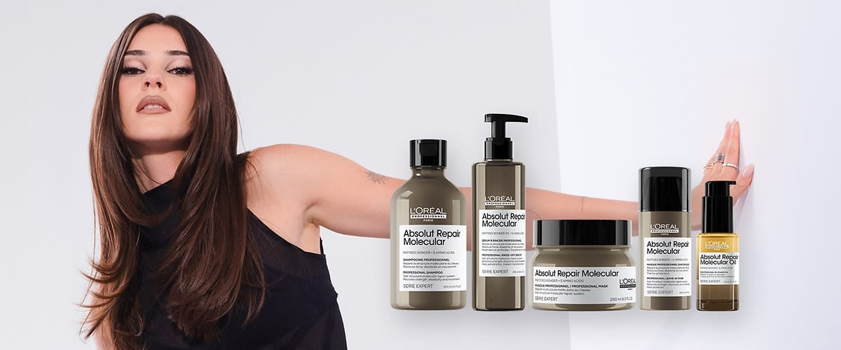 Eine junge Frau mit langen braunen Haaren und schwarzem Oberteil streckt einen Arm zur Seite, davor fünf L’Oréal Absolut Repair Molecular Haarpflegeprodukte in verschiedenen Pumpspendern und Tiegeln mit sichtbaren Produktetiketten