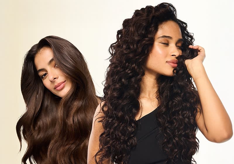 Zwei Frauen von der Brust aufwärts vor hellem Hintergrund; links glattes, langes braunes Haar über die Schulter gelegt, rechts lange, dichte Locken und leicht geschlossene Augen, beide mit dezentem Make-up und schwarzer Oberbekleidung