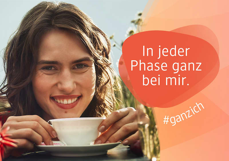Eine lächelnde junge Frau hält eine weiße Teetasse auf einer Untertasse, im rechten Bildbereich orangener Sprechblasen-Text „In jeder Phase ganz bei mir.“ und der Hashtag „#ganzich“