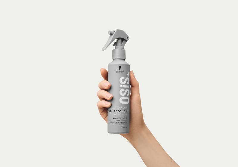 Hand hält eine grau-weiße Sprühflasche mit großer Aufschrift „OSiS“ und darunter „Curl Retouch“ als Produktbezeichnung