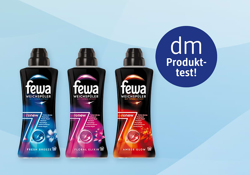 Drei schwarze Flaschen Weichspüler der Marke fewa nebeneinander: links Fresh Breeze mit blauem Etikett, Mitte Floral Elixir mit pinkem Etikett, rechts Amber Glow mit orangem Etikett, rechts oben blauer Kreis mit weißer Aufschrift dm Produkttest