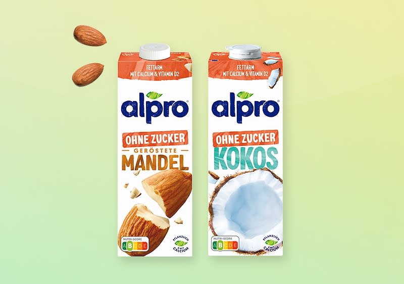 Zwei Alpro-Getränkepackungen nebeneinander vor grünem Verlaufshintergrund: links „Ohne Zucker Geröstete Mandel“ mit Mandeln und Mandelstücken abgebildet, rechts „Ohne Zucker Kokos“ mit geöffneter Kokosnuss, beide Verpackungen zeigen Alpro-Logo und Nährwertkennzeichnung