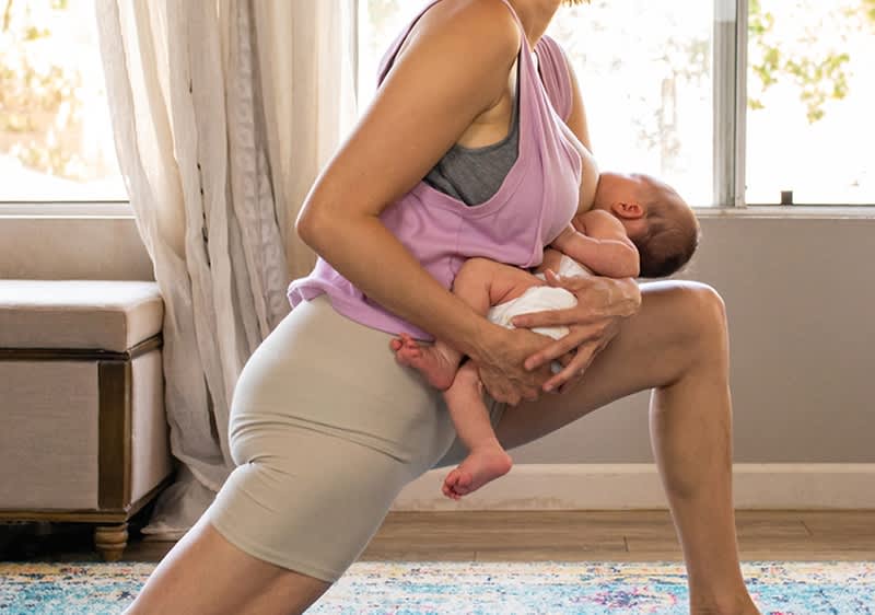 Frau macht Dehnübung mit Baby im Arm