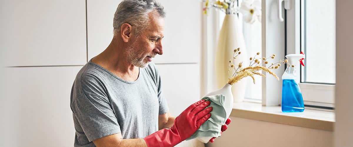 Etwas älterer Mann mit roten Putzhandschuhen putzt Vase