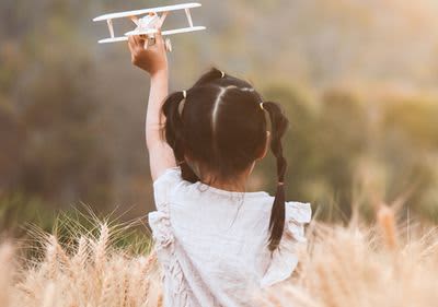 Kind in Wiese mit Spielzeugflugzeug in der Hand