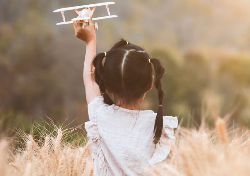 Kind in Wiese mit Spielzeugflugzeug in der Hand
