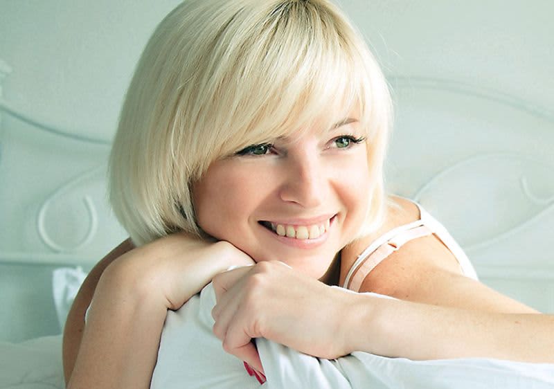 Blonde, lächelnde Frau mit weißer Bettdecke