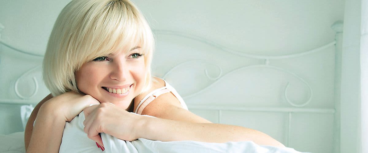 Blonde, lächelnde Frau mit weißer Bettdecke