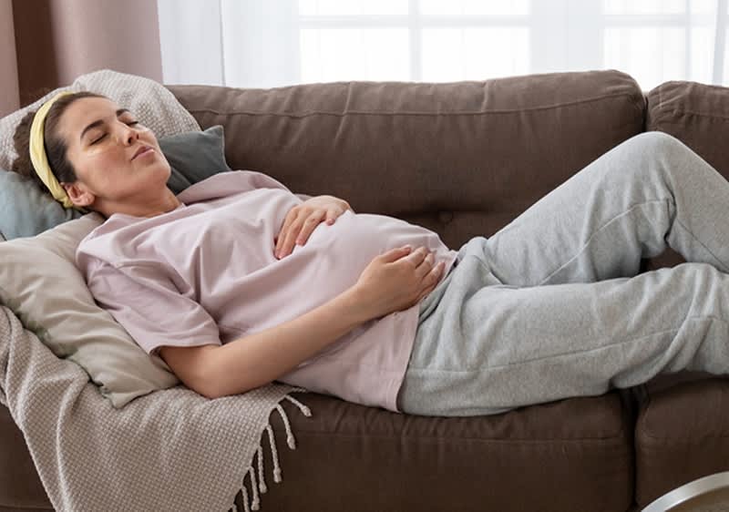Schwangere Frau in Jogginghose liegt auf dem Sofa