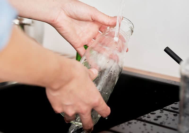 Glasflasche unter fließendem Wasser in der Küche
