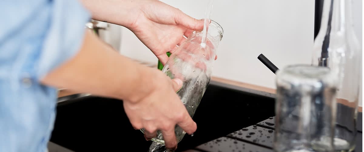 Glasflasche unter fließendem Wasser in der Küche