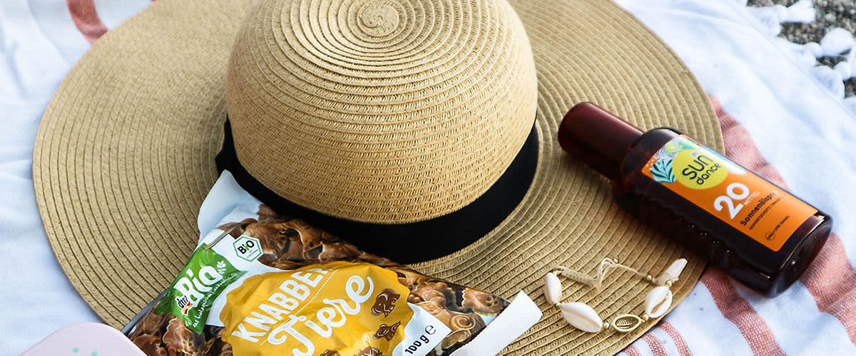 Sonnenhut, Sonnencreme und Knabber-Tierchen liegen auf einem Strandtuch.